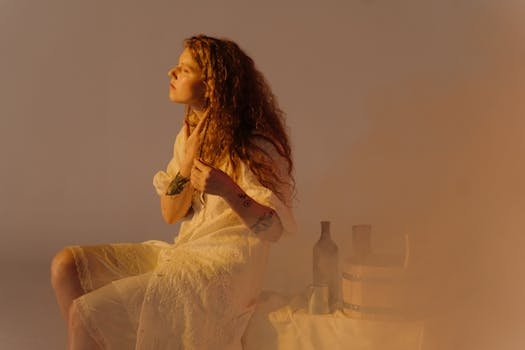 A woman with wavy hair sits thoughtfully with steam around her, wearing a white dress capturing a vintage feel.